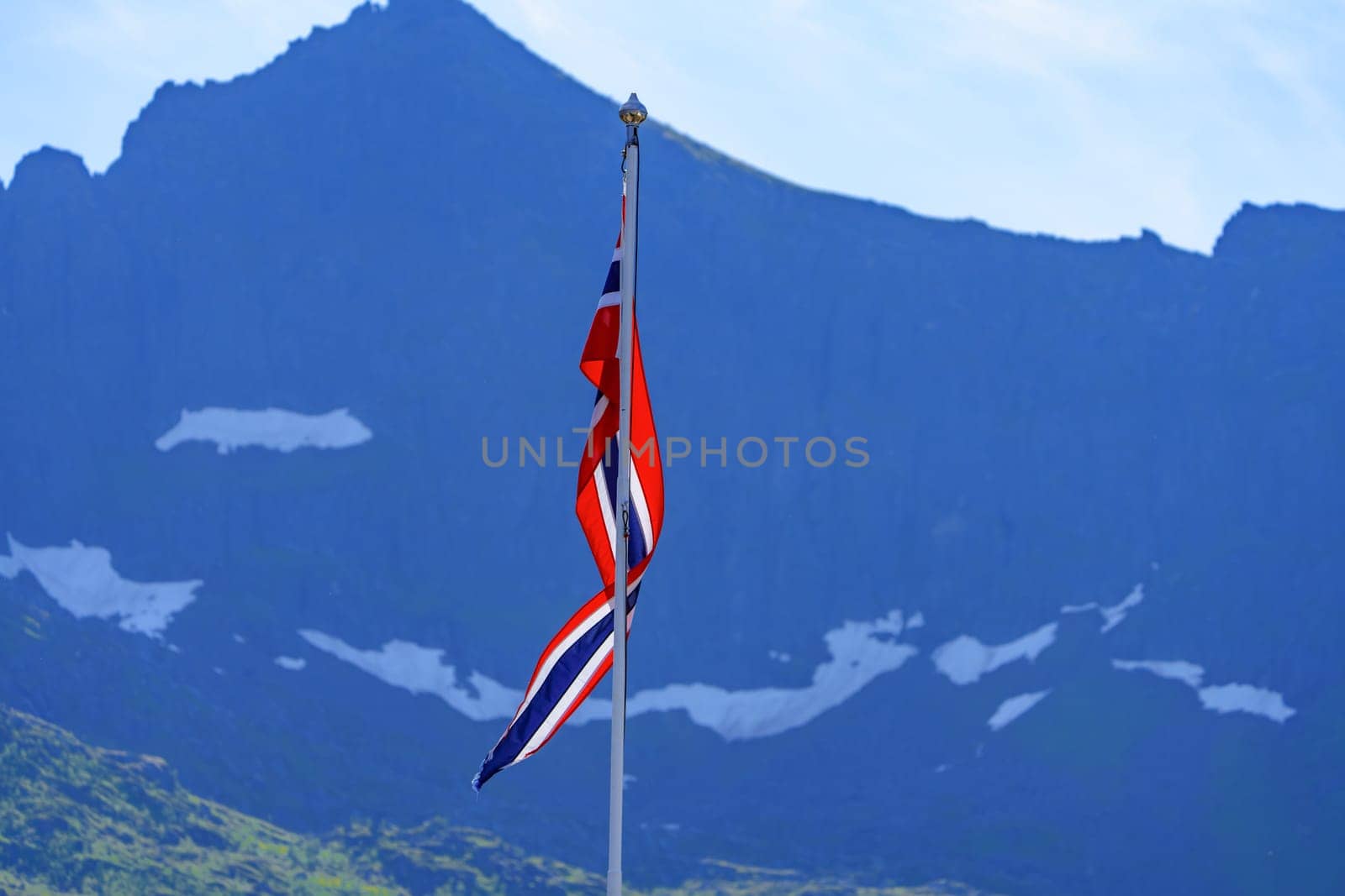 The Norwegian national flag waves proudly in front of a breathtaking mountain range, offering a stunning representation of Norway's natural beauty and national pride.