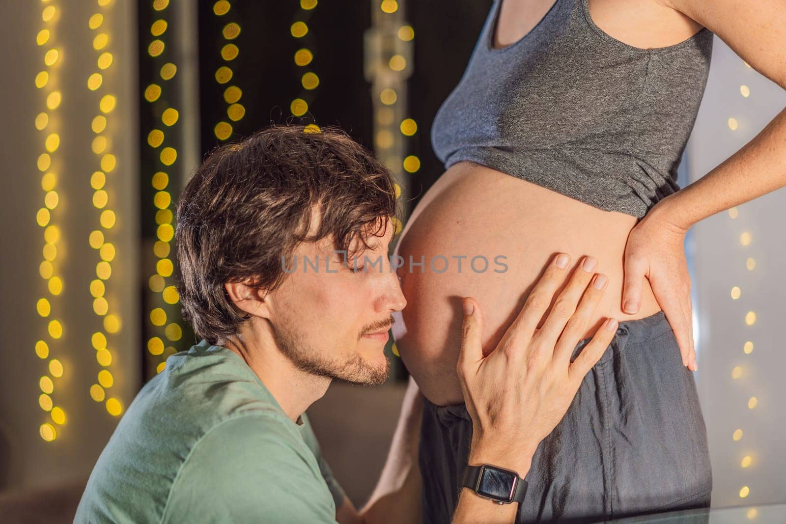 In a tender holiday moment, a husband kisses his wife's pregnant belly, expressing love and anticipation for the Christmas joy to come.