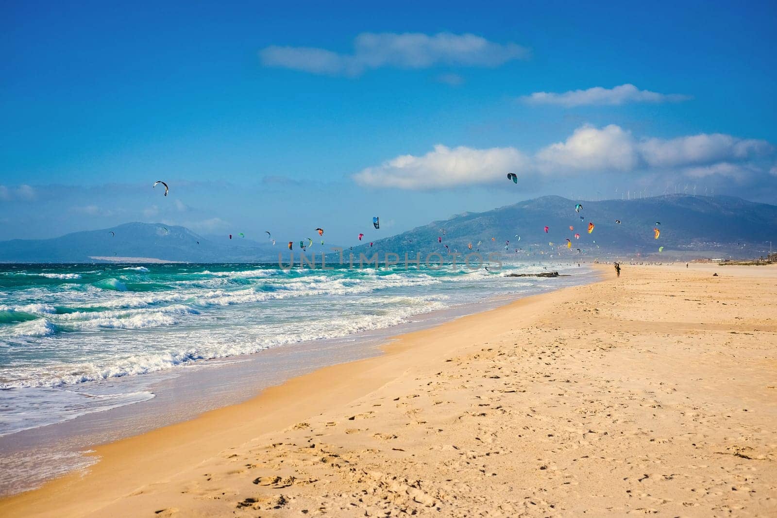 Soaring kite surfers and beach with Atlantic ocean and golden sand on background of mountains. Spain Tarifa