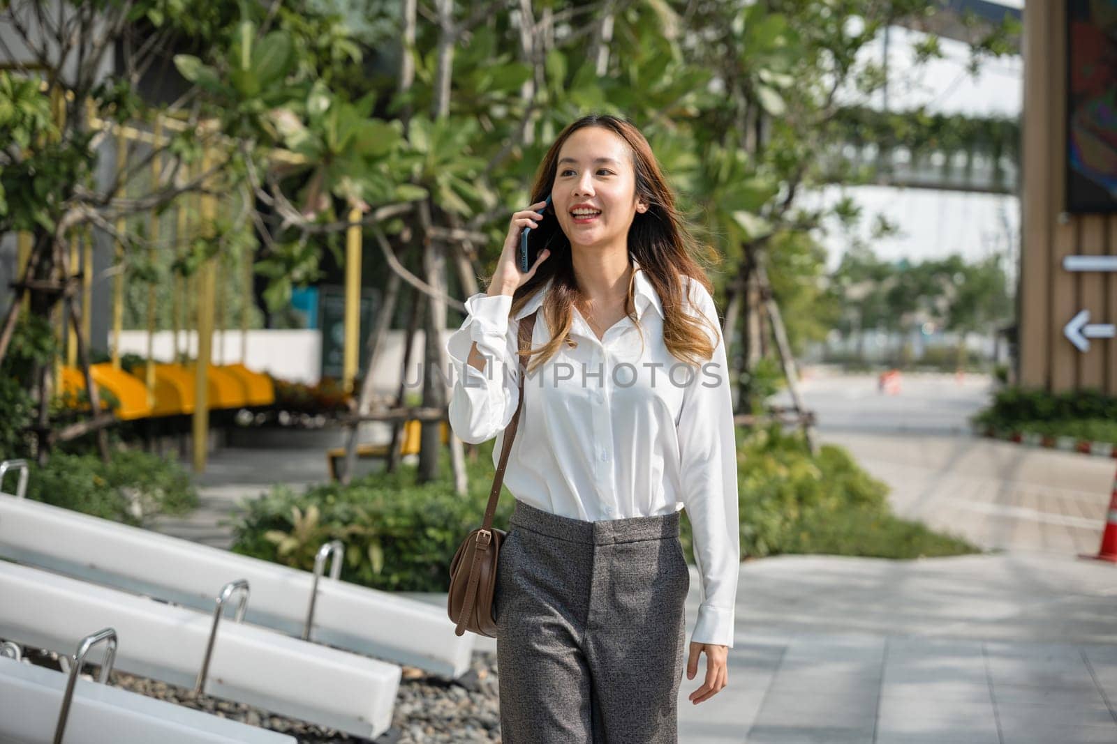 Asian business female calling on smart mobile phone and walking on street outside office building by Sorapop