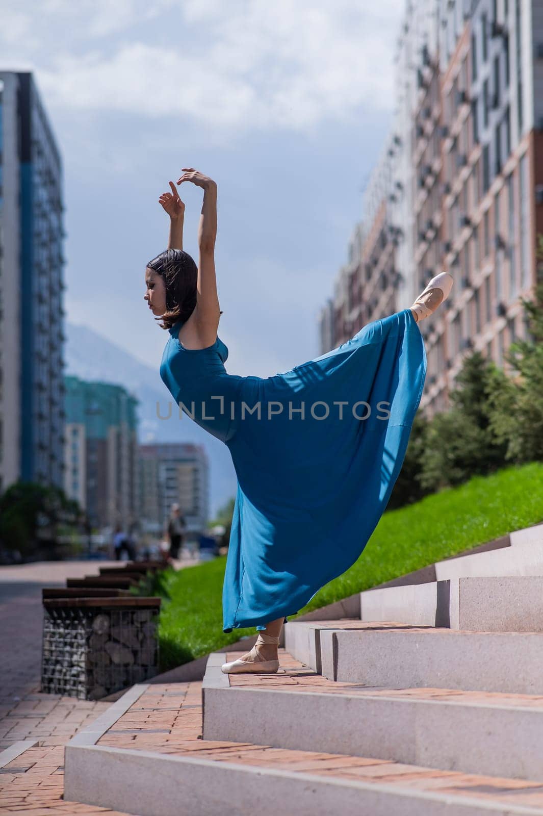 Beautiful Asian ballerina in blue dress posing on stairs outdoors. Urban landscape. Vertical photo. by mrwed54