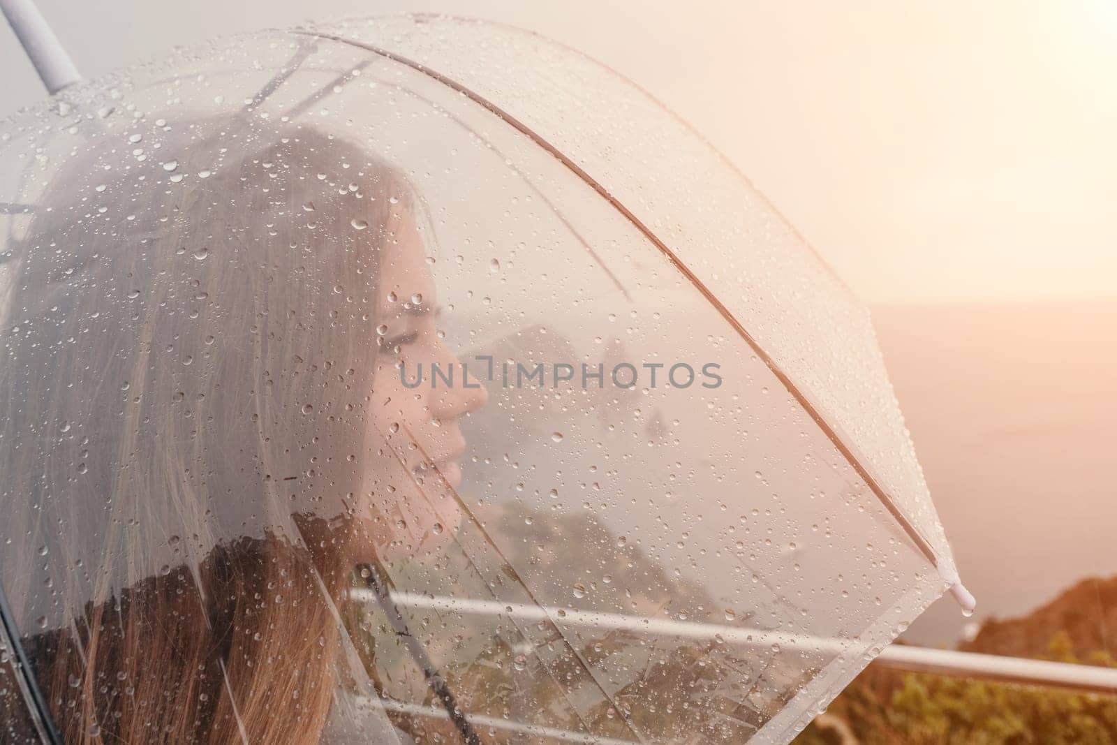 Woman rain umbrella. Happy woman portrait wearing a raincoat with transparent umbrella outdoors on rainy day in park near sea. Girl on the nature on rainy overcast day. by panophotograph