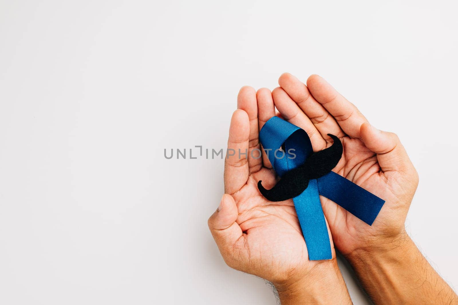 Supporting men living with cancer in November. A man's hands cradle a light blue ribbon with a mustache on a blue background, representing unity and strength.