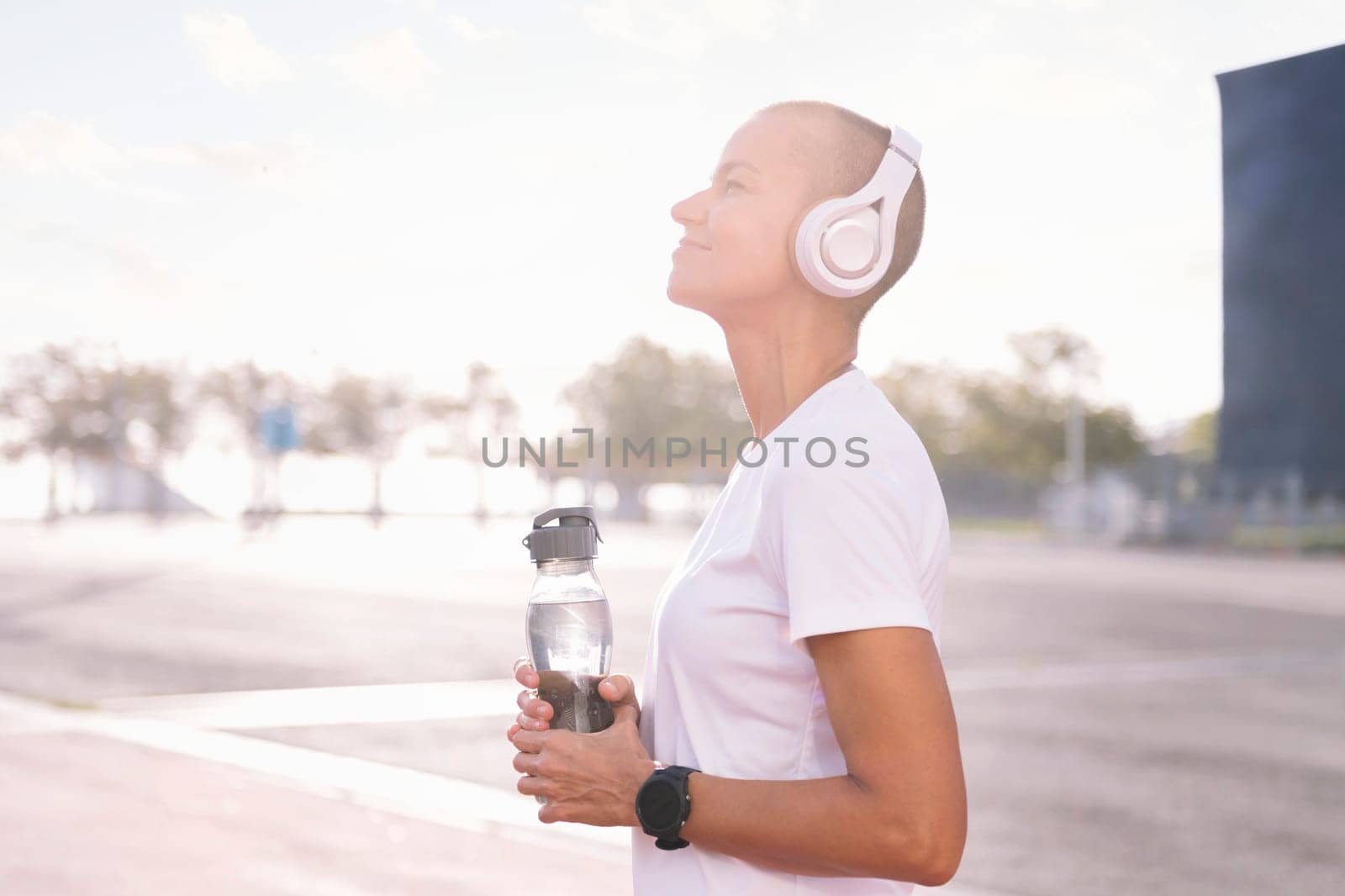 young sports woman smiling happy with a bottle in her hand listening to music on her headphones, concept of active and healthy lifestyle, copy space for text