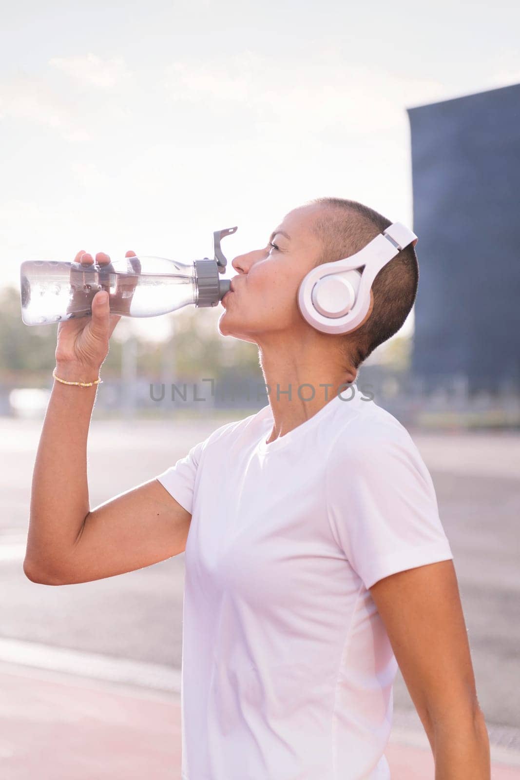 young sports woman drinking water from her bottle and listening to music on her headphones, concept of active and healthy lifestyle, copy space for text