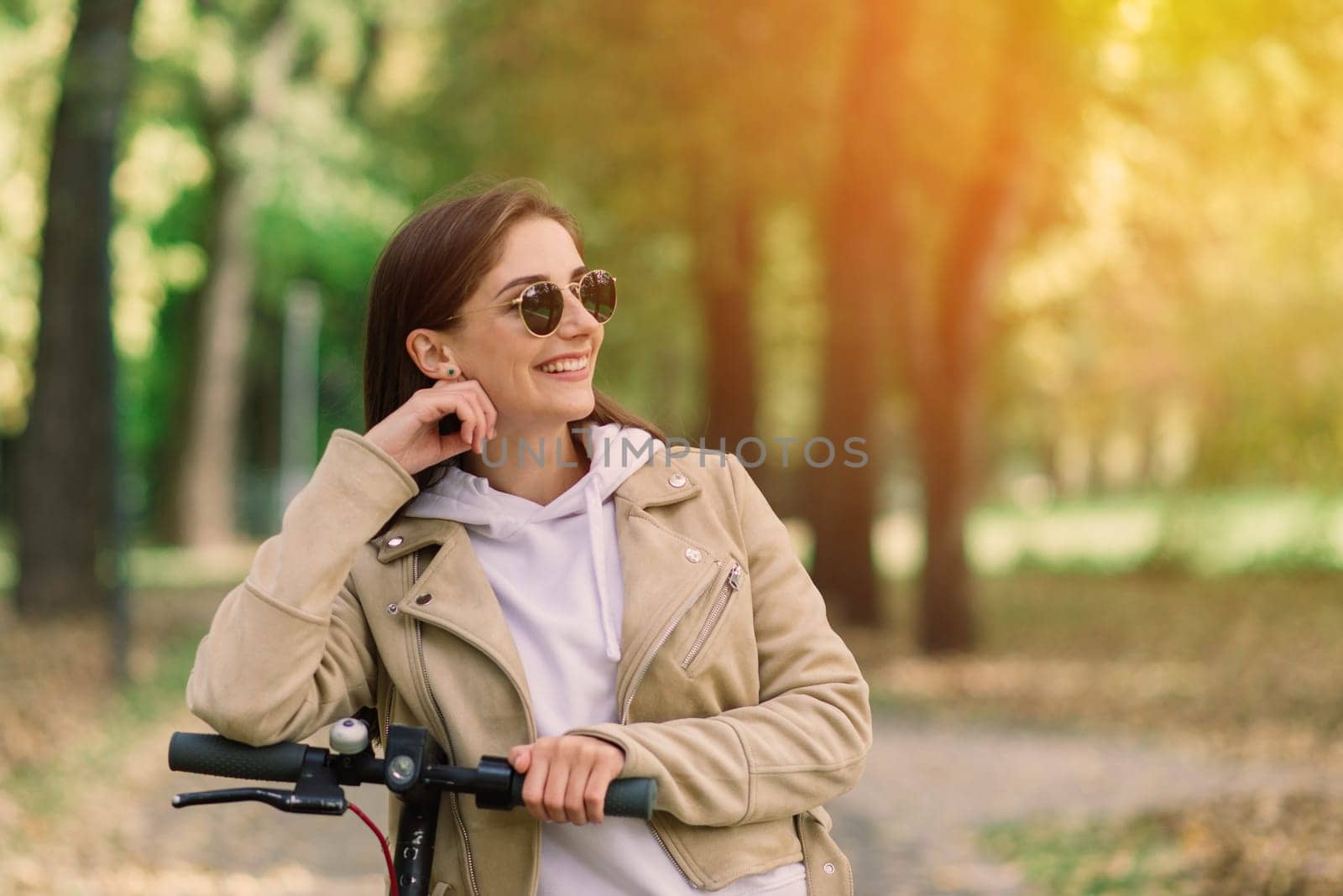 Young woman riding an electric scooter in autumn park. Green transport, traffic jam problems.