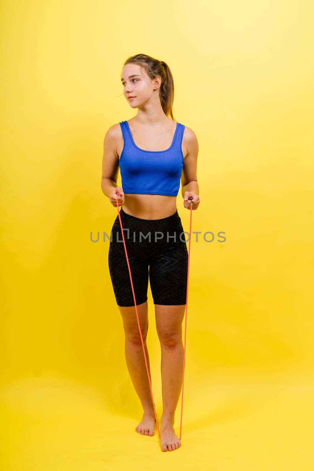 Portrait of gentle muscular woman holding skipping rope on her neck over yellow background