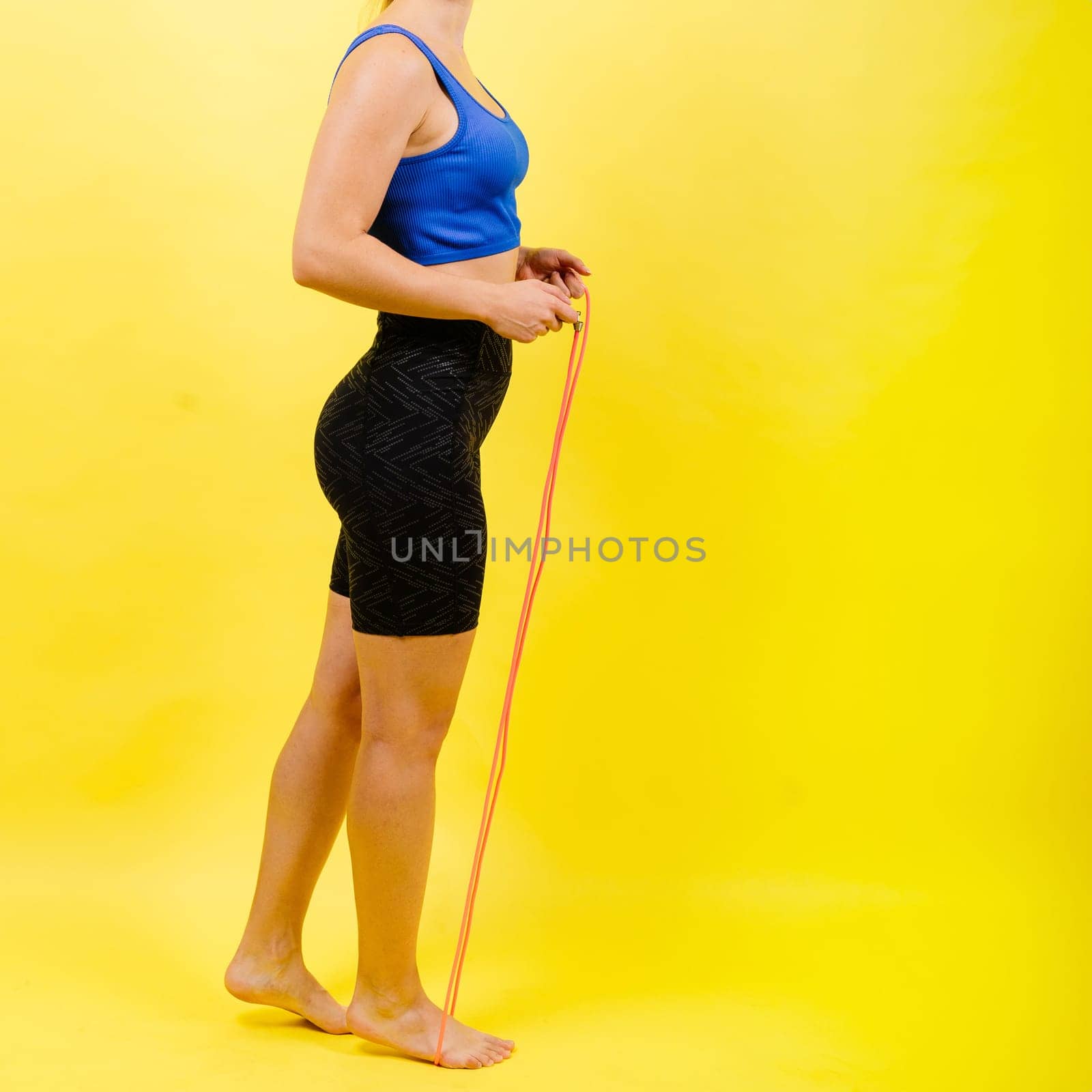 Portrait of gentle muscular woman holding skipping rope on her neck over yellow background