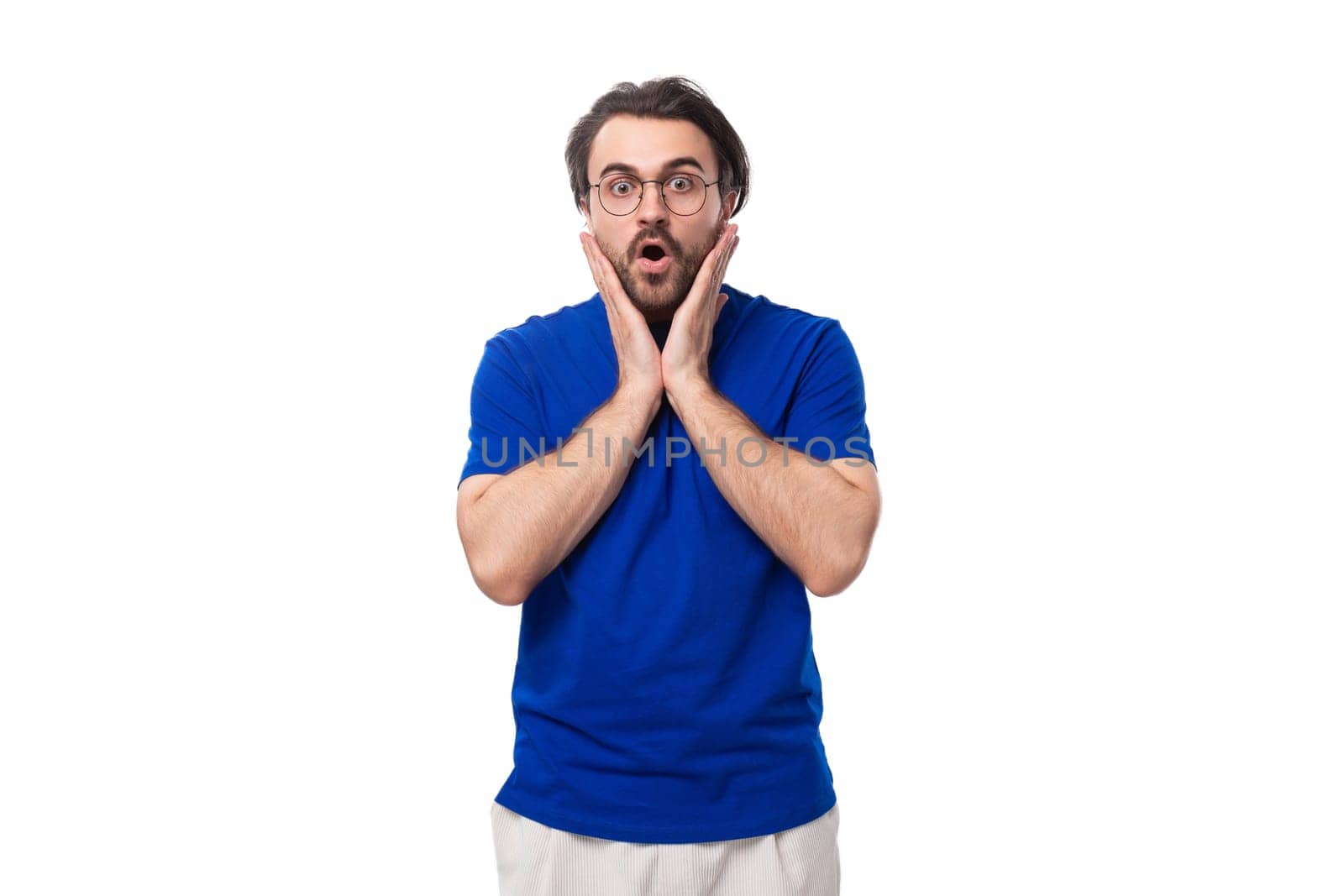 30 year old surprised european brutal guy with black hair and a beard in a blue t-shirt on a white background with copy space.