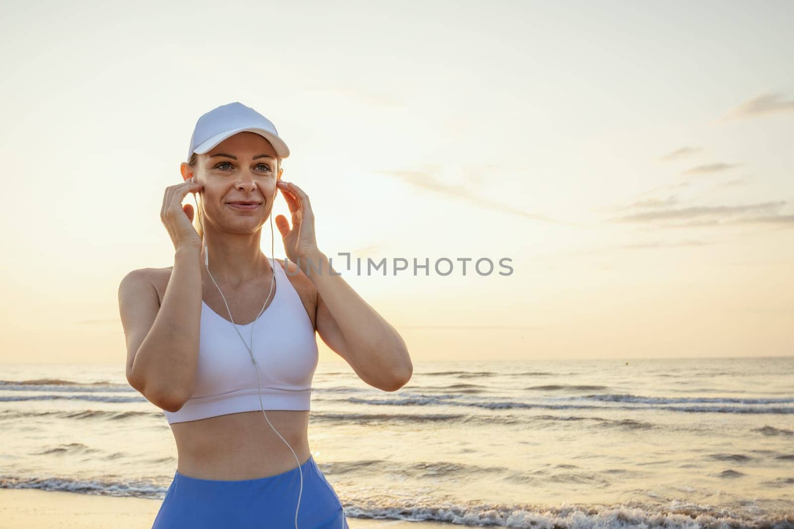A girl of European appearance in a white cap stands against the background of the sea wearing headphones, there is a place for an inscription High quality photo