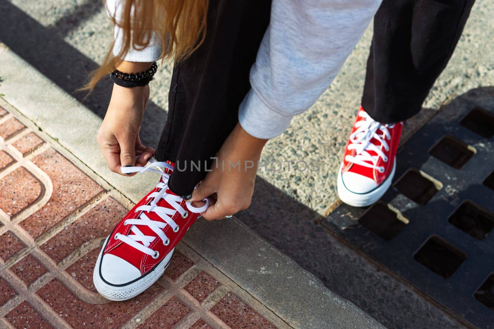 Outdoor lifestyle close up of the legs of a beautiful teenage girl. Young hipster woman tying laces in red sneakers. Sunny hot summer day. High quality photo