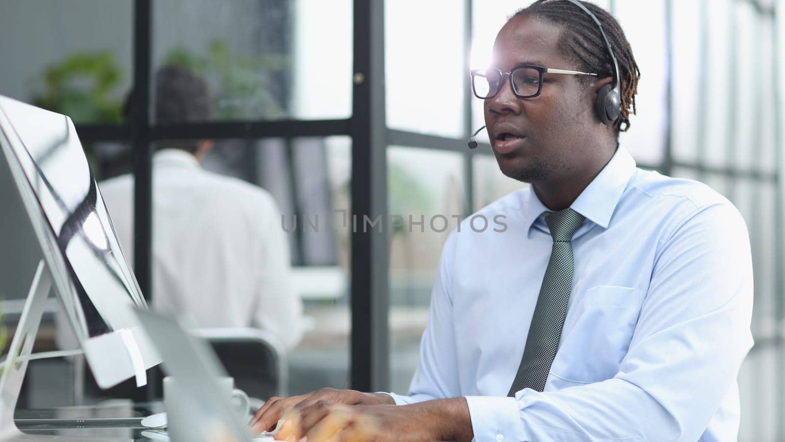 a man at a computer in a call center talking using headphones with a microphone by Prosto
