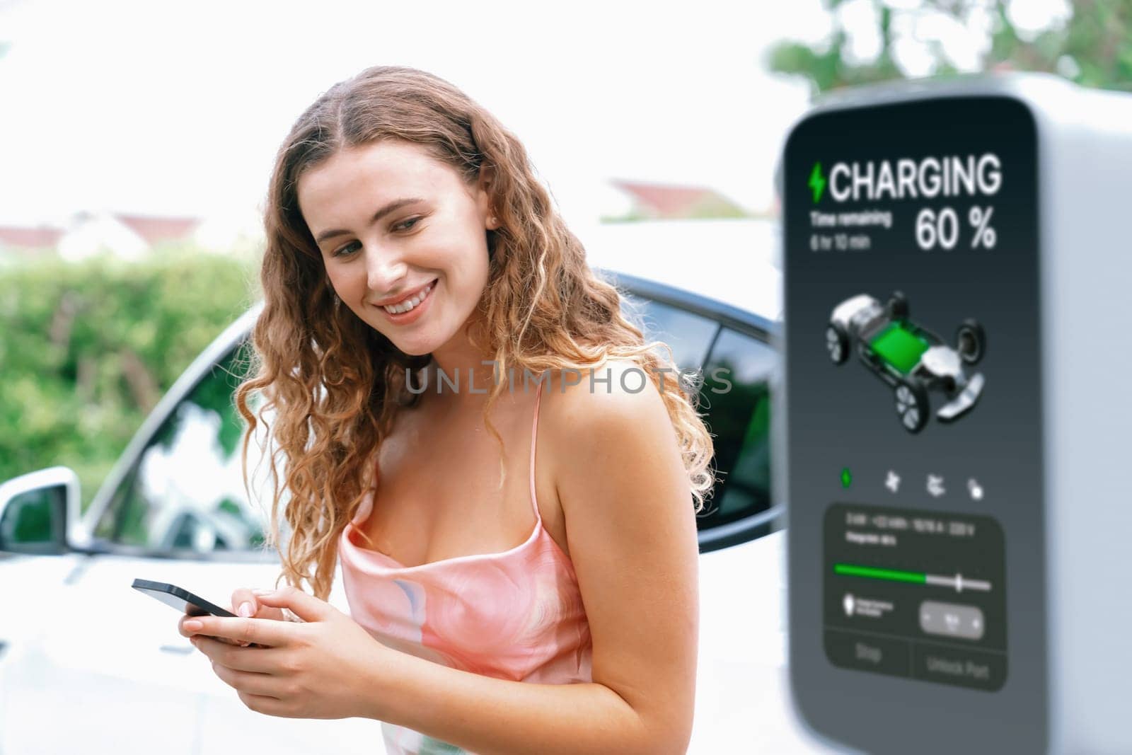 Modern eco-friendly woman recharging electric vehicle from EV charging station. Innovative EV technology utilization for tracking energy usage to optimize battery charging. Synchronos