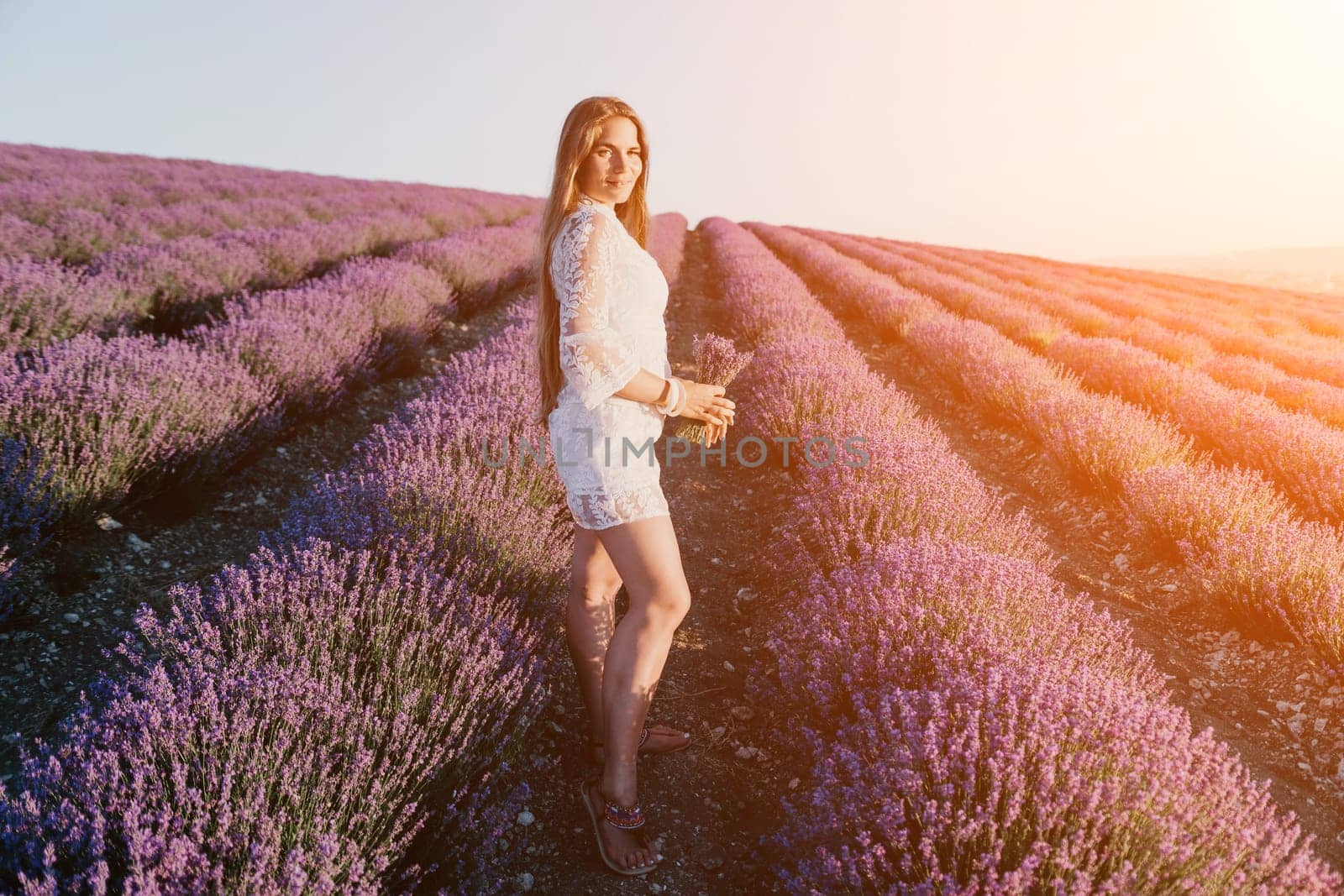 Woman lavender field. Happy carefree woman in a white dress walking in a lavender field and smelling a lavender bouquet on sunset. Ideal for warm and inspirational concepts in wanderlust and travel. by panophotograph