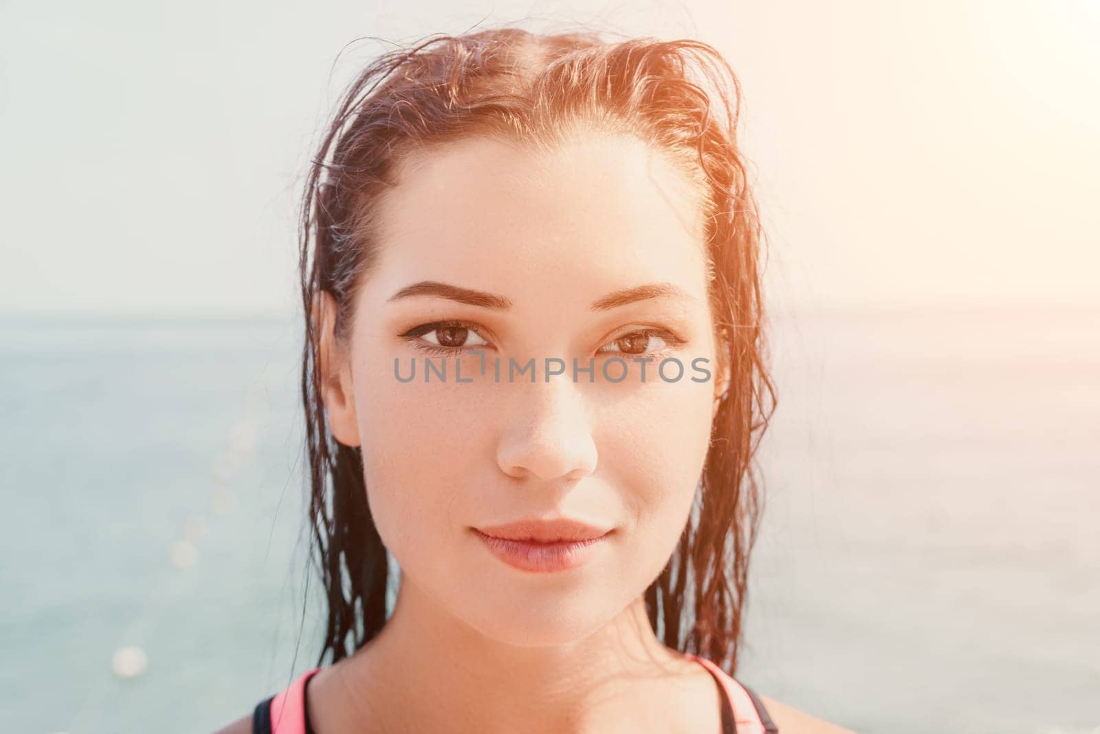 Close up shot of beautiful young caucasian woman with black hair and freckles looking at camera and smiling. Cute woman portrait in a pink bikini posing on a volcanic rock high above the sea