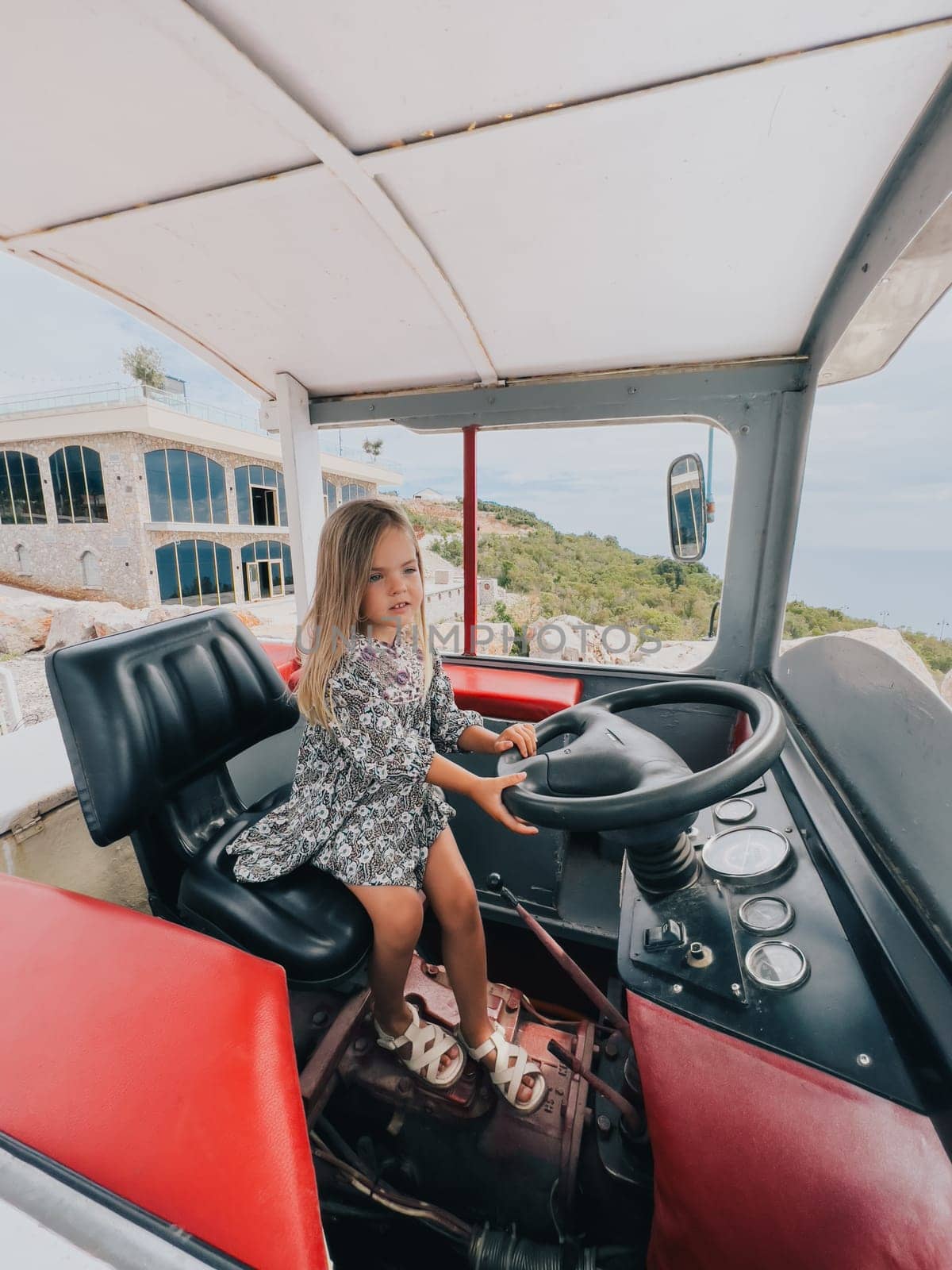 Little girl sits behind the wheel of a tractor in the cab. High quality photo