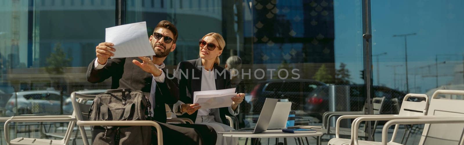 Business colleagues working with documents sitting outside of office on cafe terrace by Yaroslav_astakhov