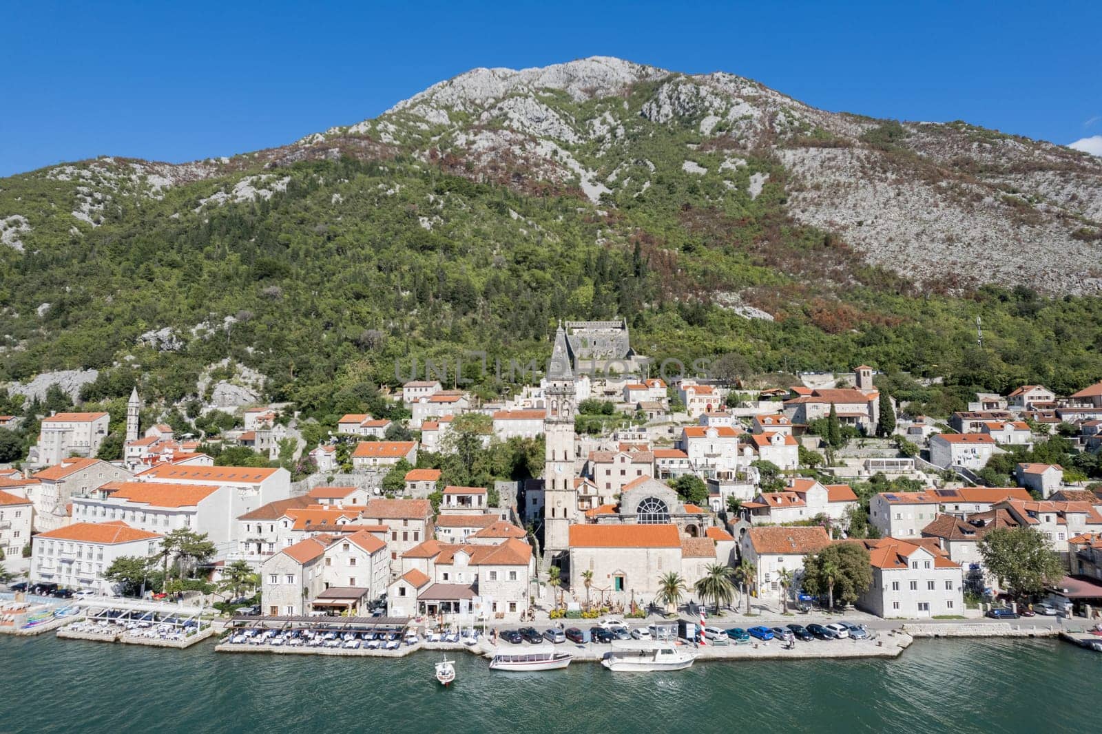 Motor boats stand off the coast of Perast against the backdrop of the Church of St. Nicholas and ancient houses. Montenegro by Nadtochiy