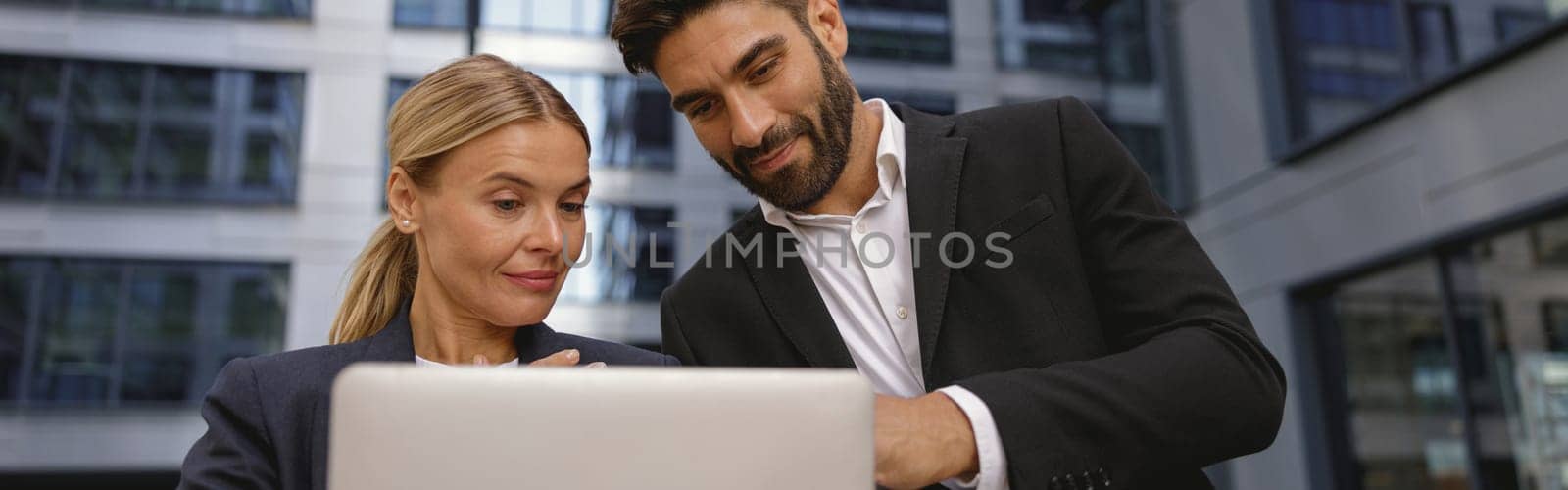 Focused business colleagues discuss biz issue while use laptop standing on office terrace by Yaroslav_astakhov