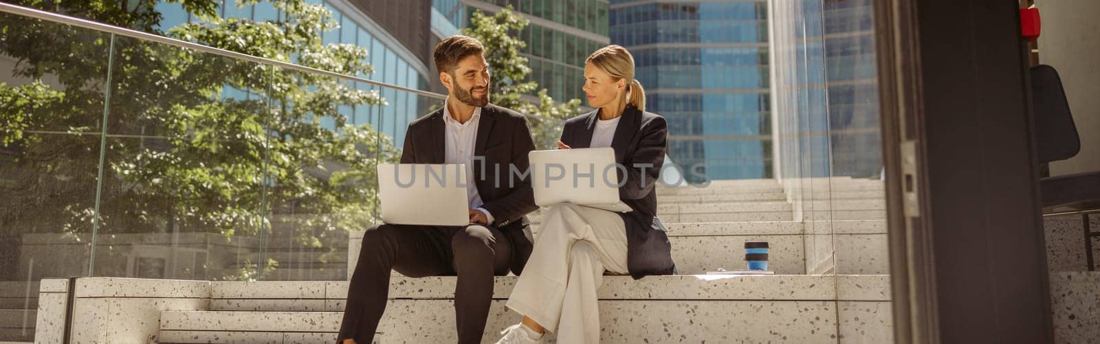 Contemporary businessman and businesswomen working outdoor on laptop with new startup project by Yaroslav_astakhov