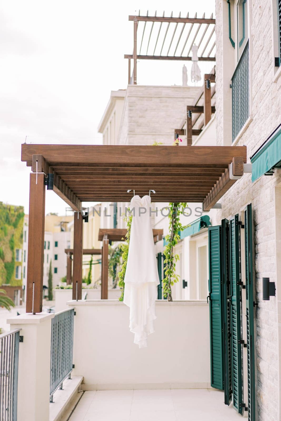 White bride dress with a long train hangs on a hanger on a wooden cover on a hotel balcony. High quality photo