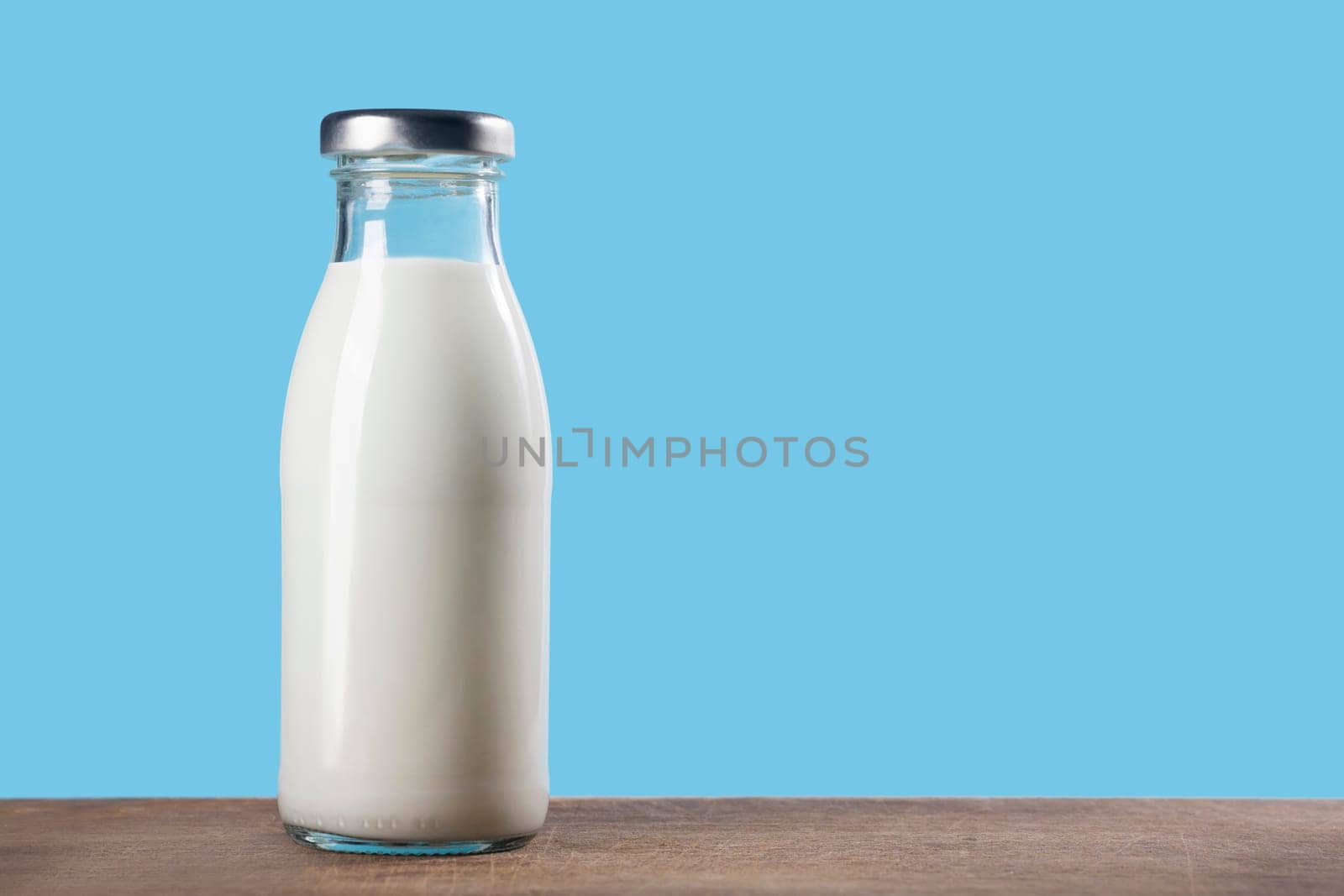 Bottle of milk on a wooden table on a blue background.