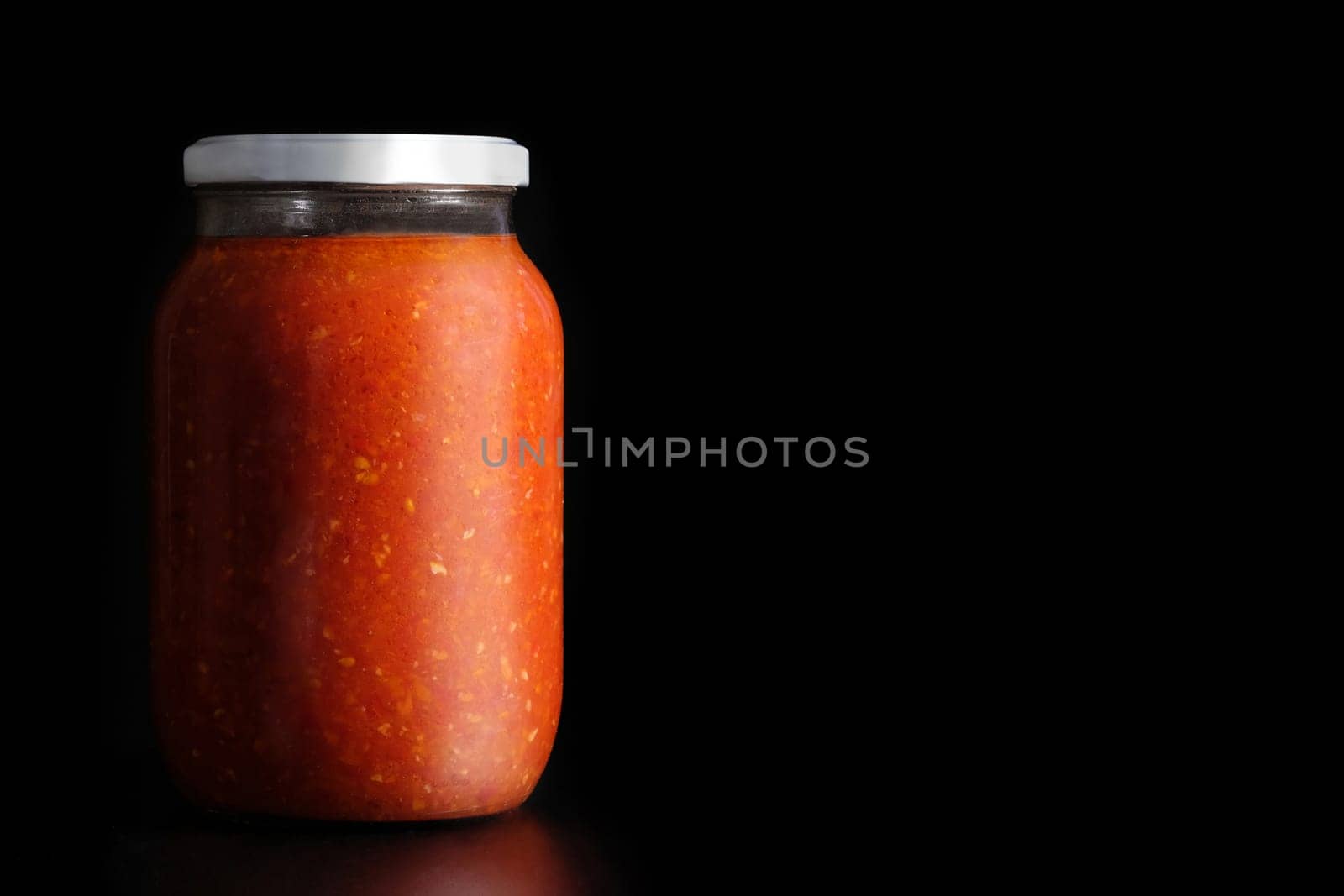 Glass jar of canned food on a black background, with copy space. by Shablovskyistock