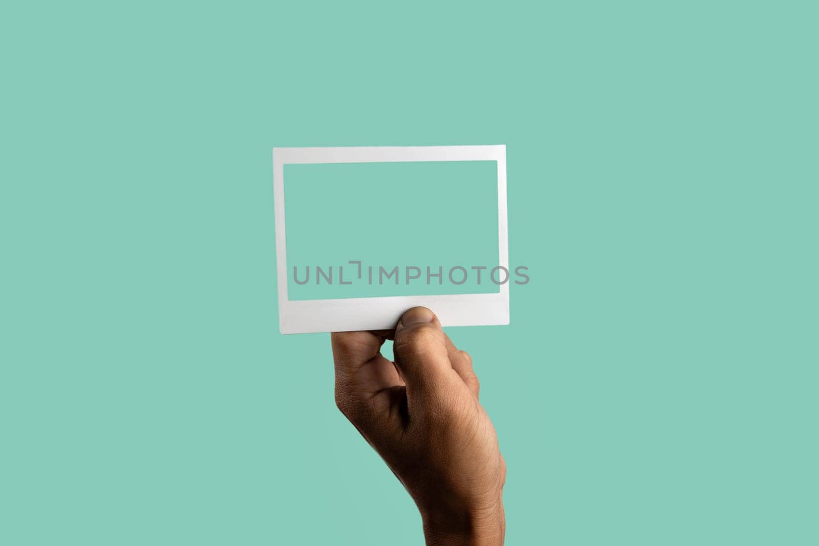 black male hand holding photo frame on isolated white on turquoise background by TropicalNinjaStudio