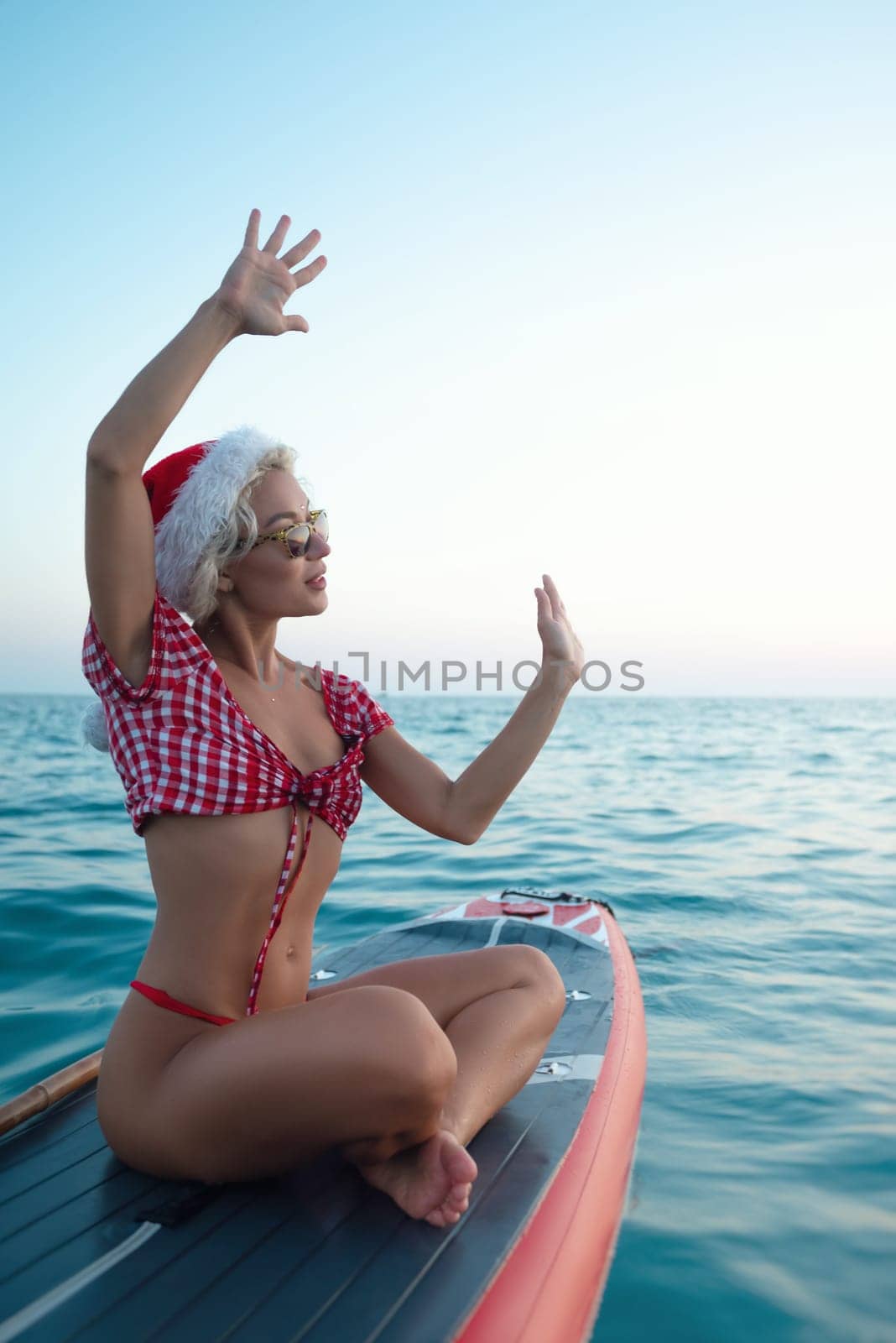 A sexy girl in a Santa Claus hat floats on the sea on a Sup board relaxes and meditates enjoys life and relaxation at sea