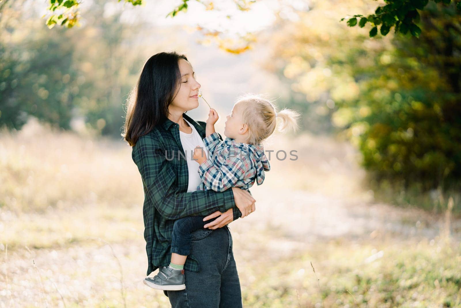 Little girl gives a flower to her mother to smell while sitting in her arms. High quality photo