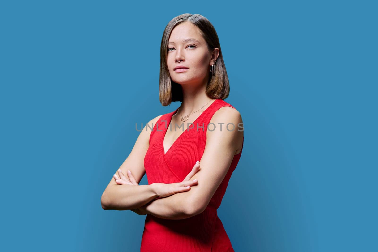 Young serious confident woman in red on blue studio background by VH-studio