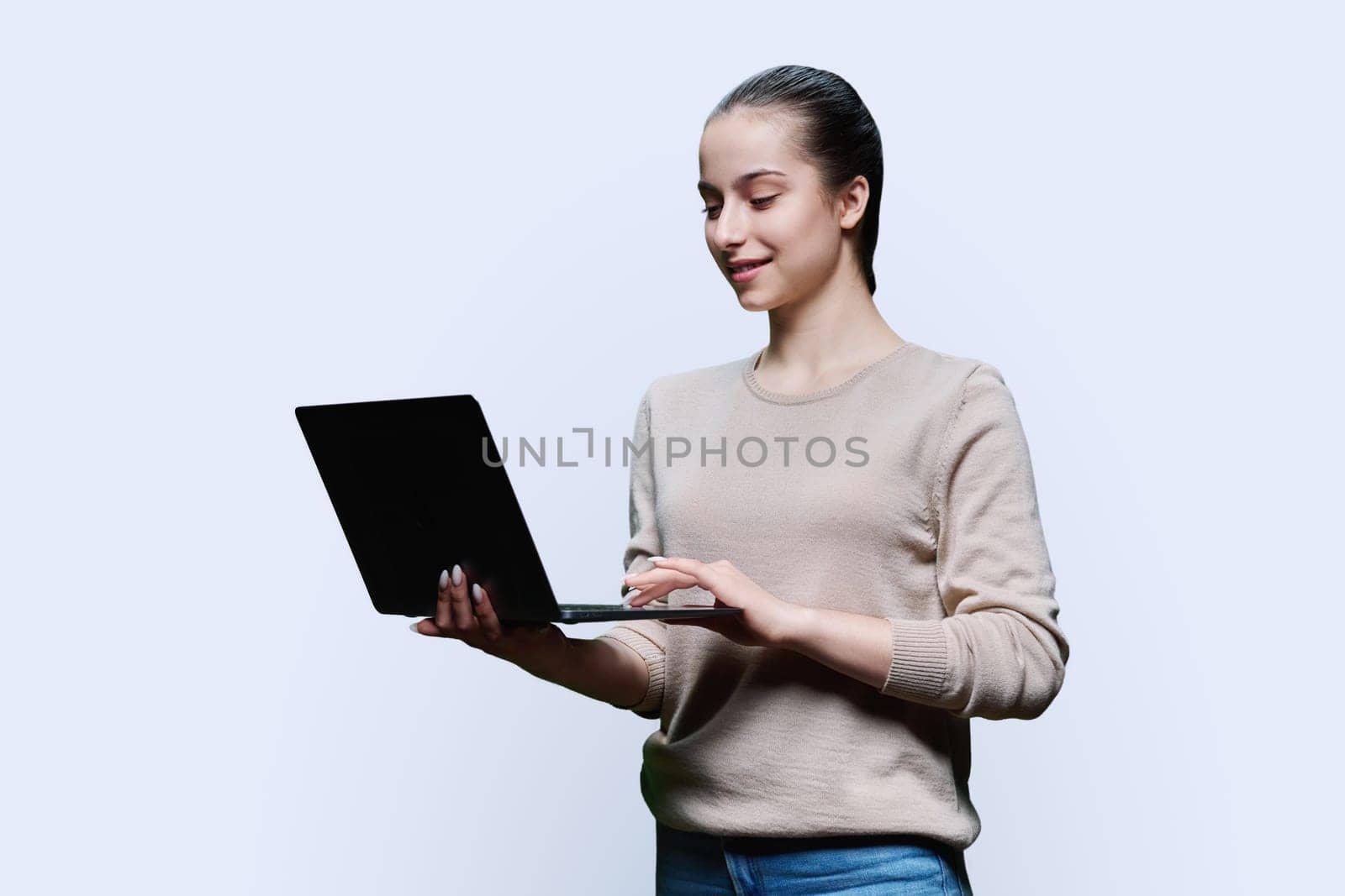Teen girl high school student using laptop looking at computer screen, on white studio background. Technology, e-learning, education, adolescence, youth concept.