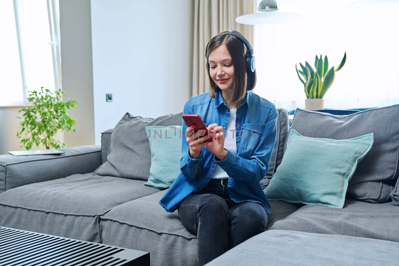 Young woman in headphones listening music audio book, chatting, sitting at home by VH-studio