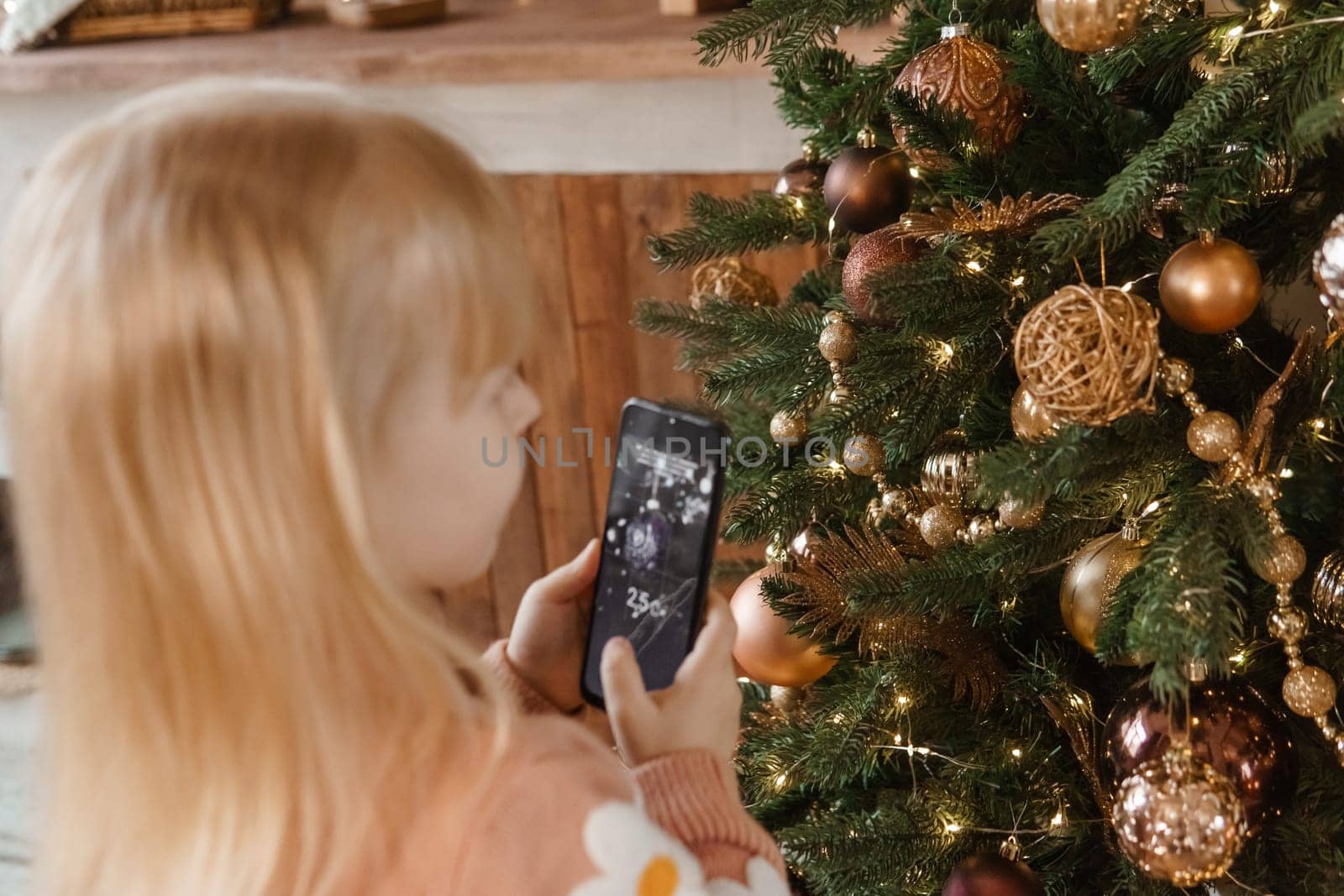 A little blonde girl photographs balloons on a Christmas tree in a festive interior decorated in a New Year's style. The concept of a merry Christmas