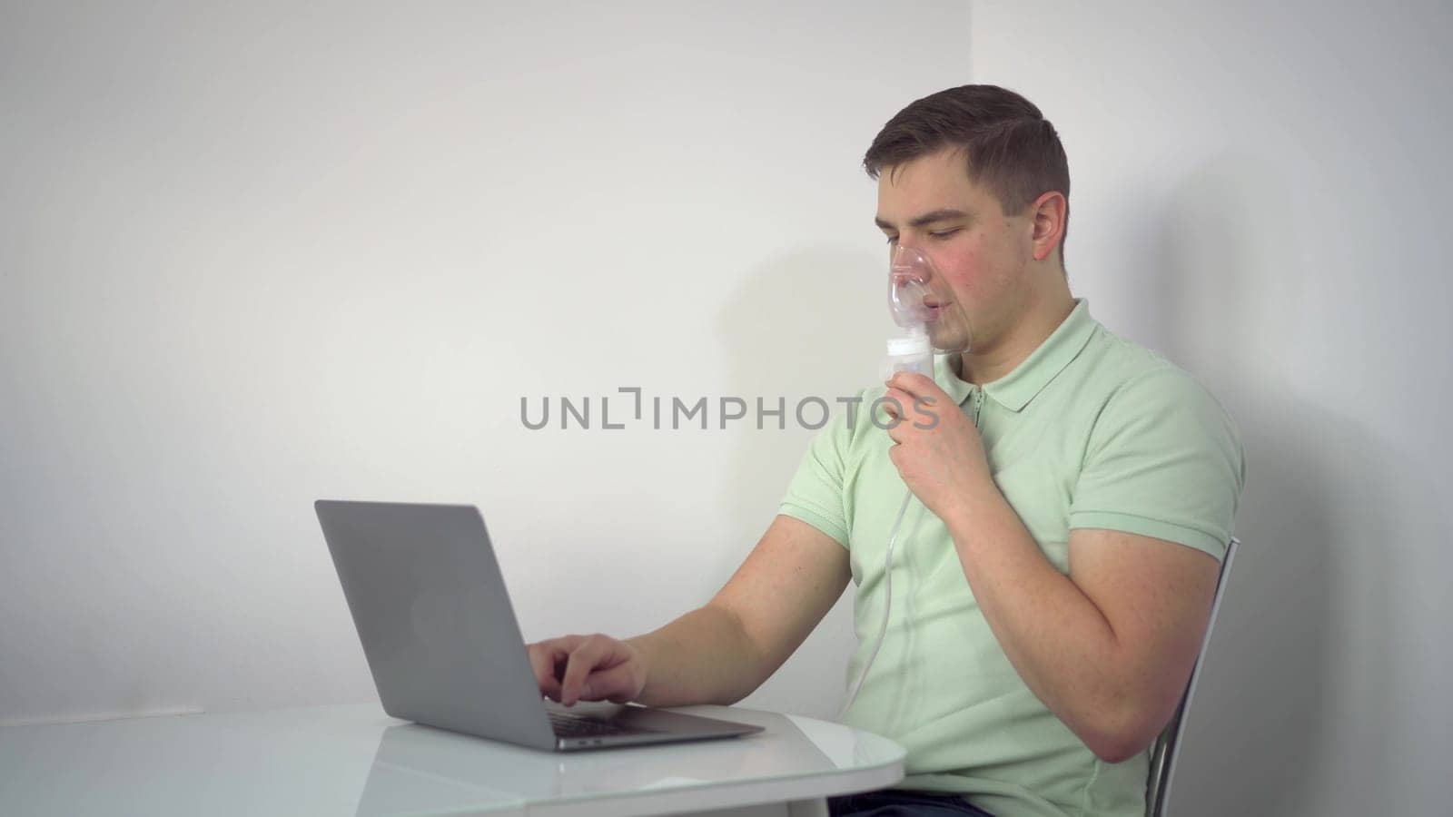 A young man breathes through an inhaler and uses a laptop. A man with an oxygen mask is being treated for a respiratory infection and typing on a netbook. 4k