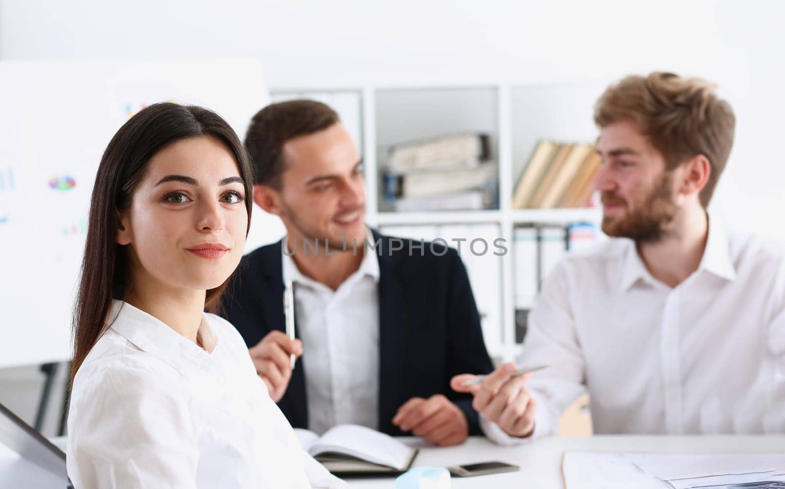 Beautiful smiling cheerful girl at workplace look in camera with colleagues group in background. White collar worker at workspace job offer modern lifestyle client visit profession train concept