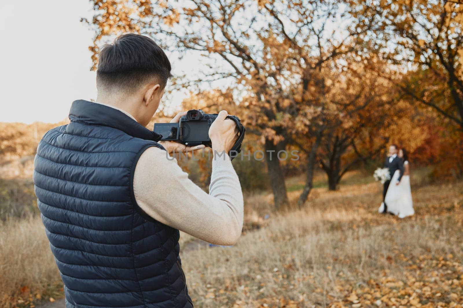 Professional wedding photographer taking pictures of the bride and groom in nature in autumn