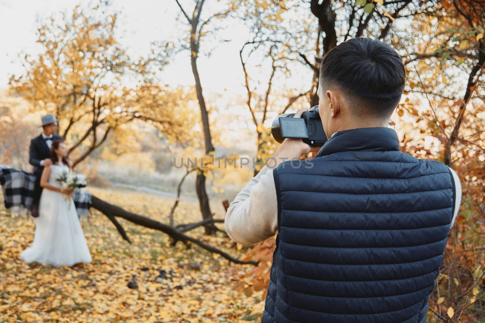 Professional wedding photographer taking pictures of the bride and groom in nature in autumn