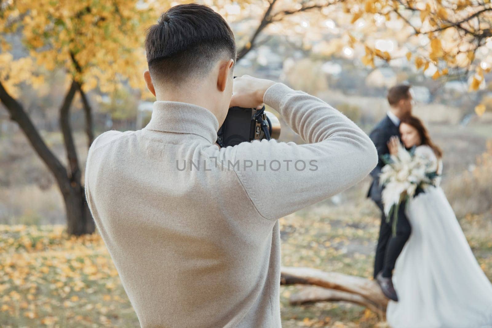 Professional wedding photographer taking pictures of the bride and groom in nature in autumn