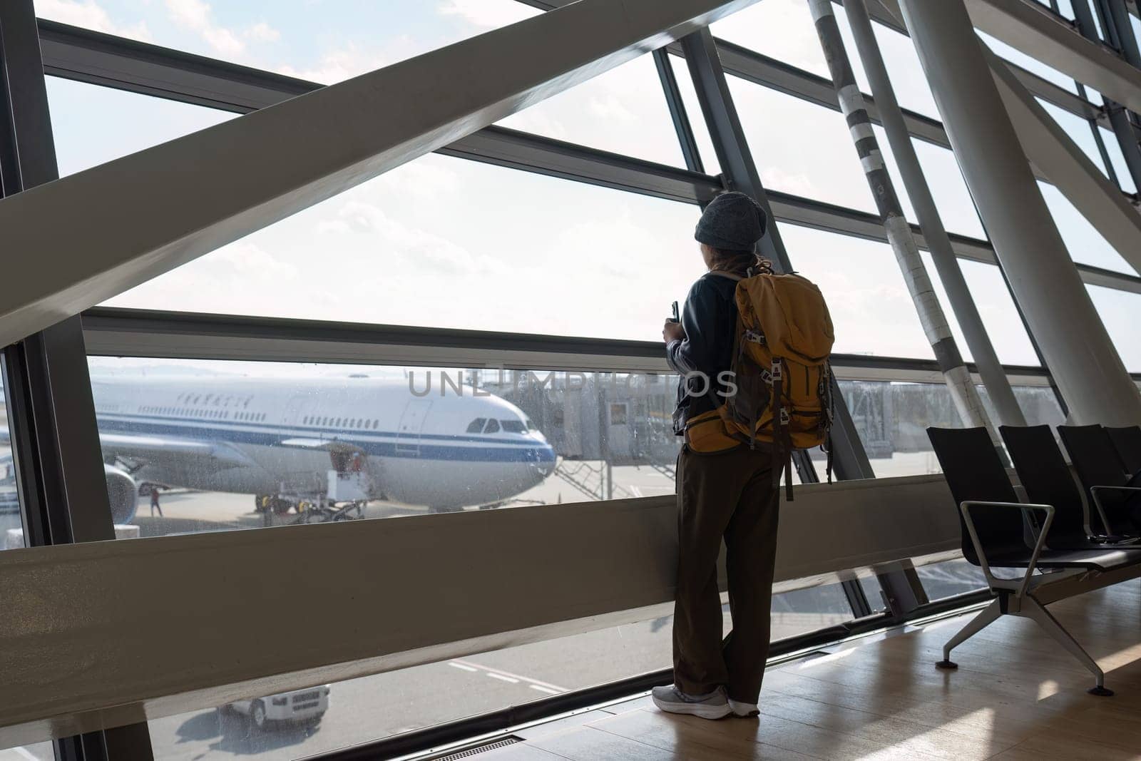 Traveler woman plan and backpack see airplane flight at the airport glass window.