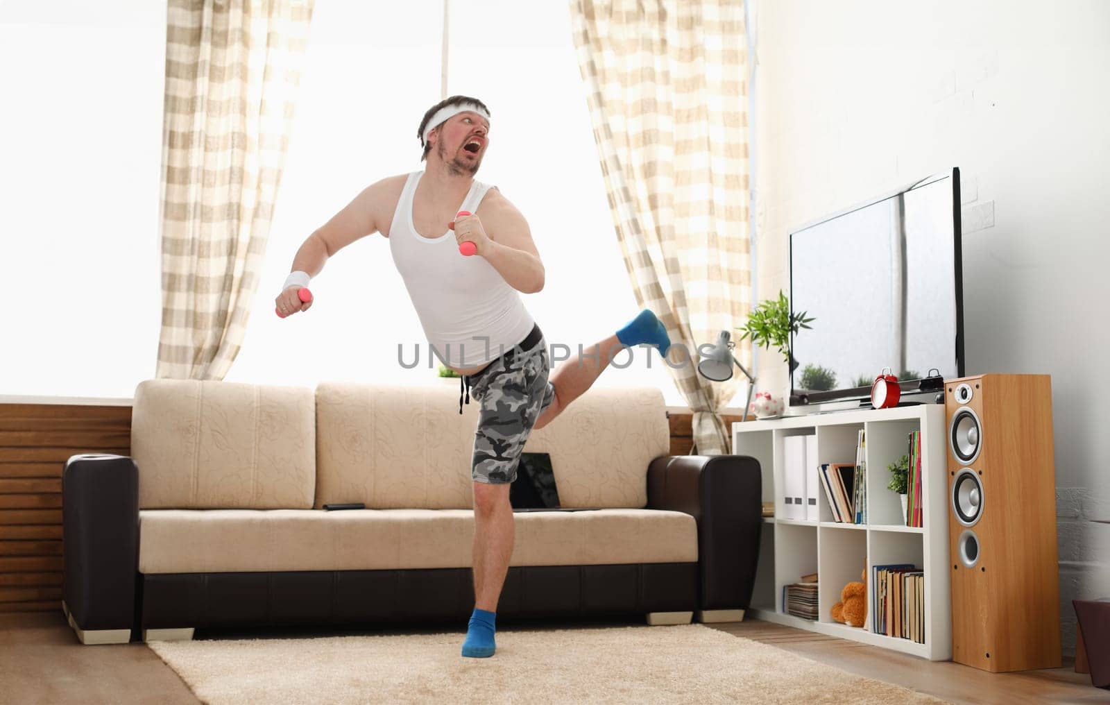 Young handsome man in shorts and vest holds pink dumbbells in hand. Watch tv lessons single combats is practicing receptions of sensei one home fitness indoor training independent education remotely
