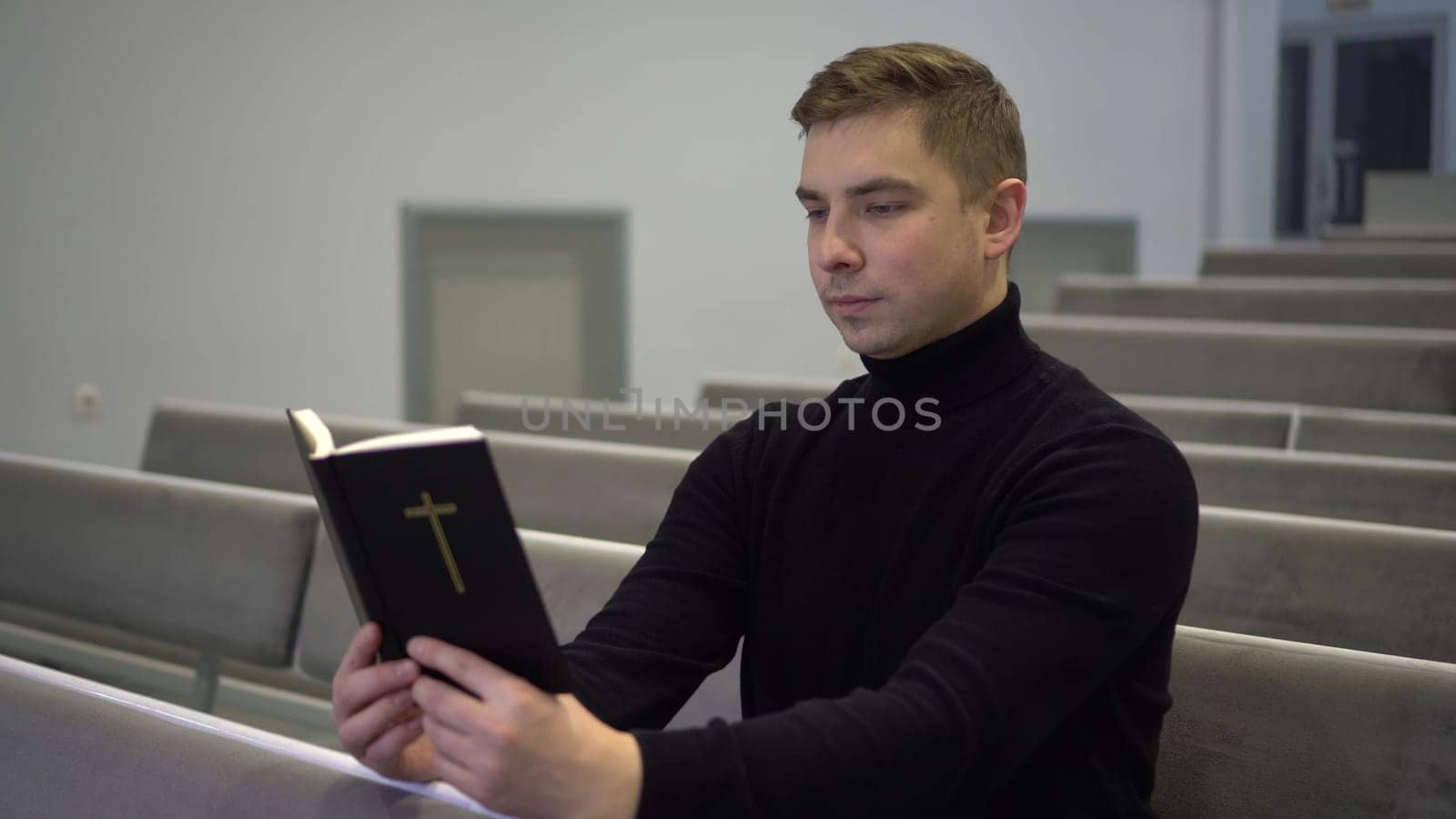 A young man reads the Bible while sitting on a church bench. A Protestant man reads the Bible in church. by Puzankov