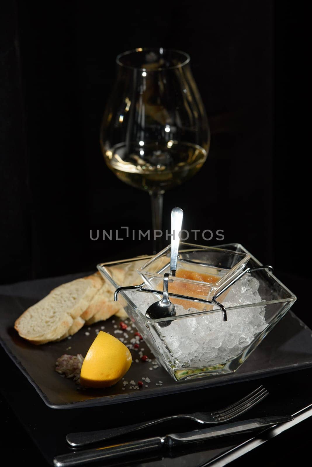 Pike fish caviar, on ice, with croutons, lemon, on a transparent dish, on a dark background by Ashtray25