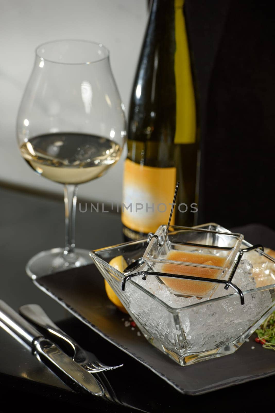 Pike fish caviar, on ice, with croutons and butter, on a transparent dish with a glass of white wine on a dark background