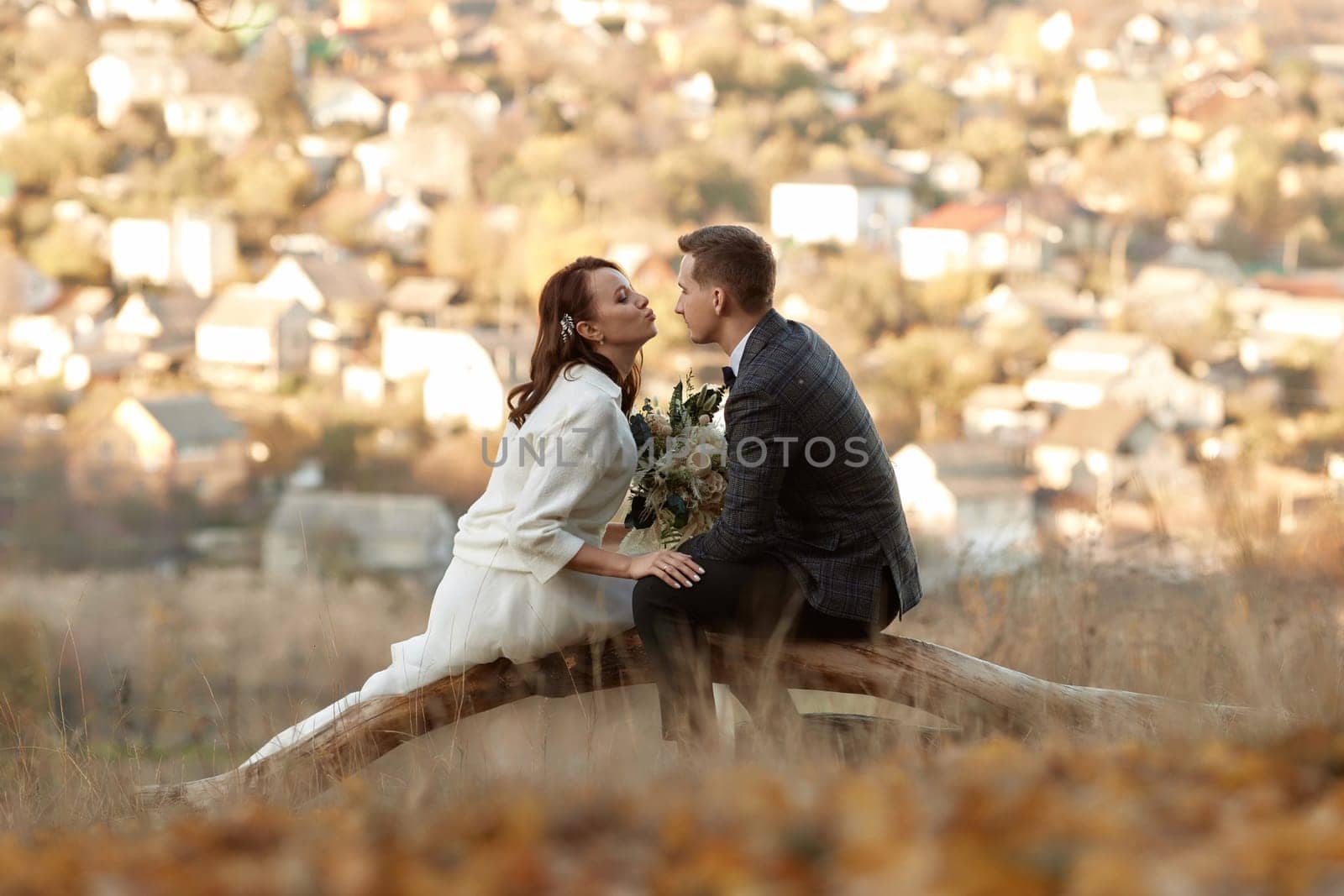 bride in white wedding dress and groom are sitting on tree by erstudio