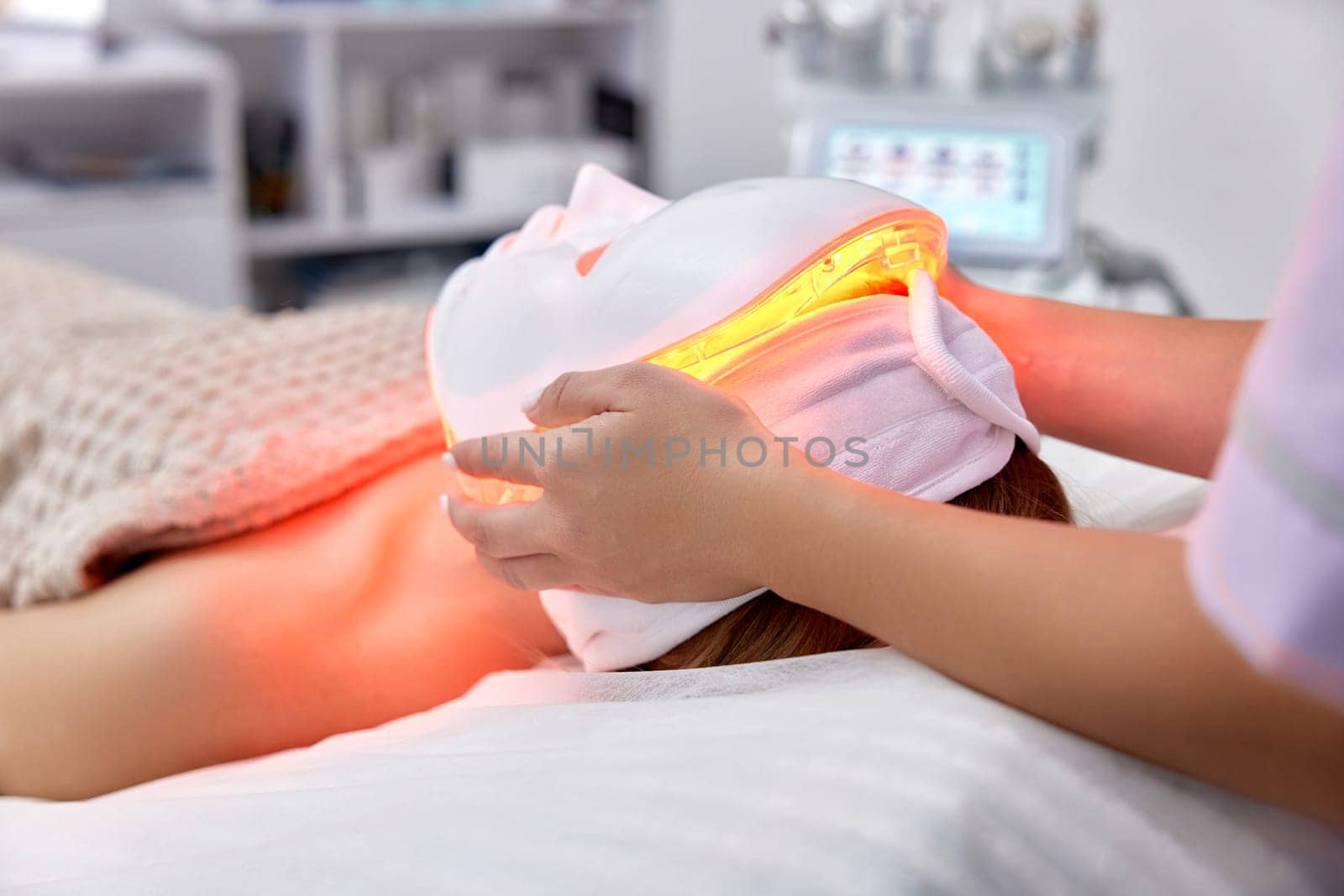 woman receiving led light anti-aging mask treatment from beautician in beauty salon