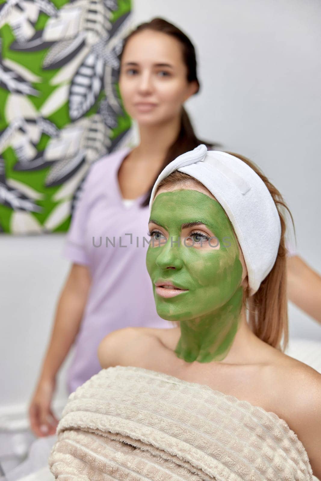female cosmetologist and woman client with facial mask in beauty clinic.