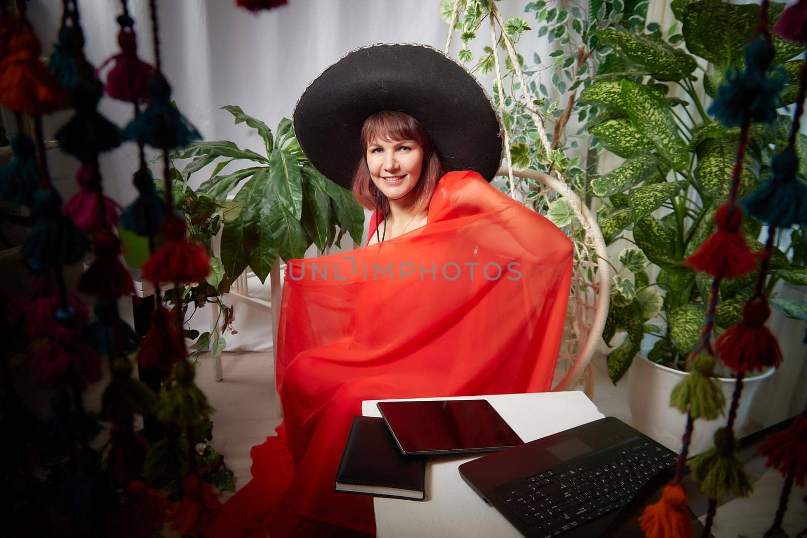 Funny, cute, self-confident adult girl posing in red dress and a huge hat in the room. A middle-aged model at a photo shoot in the studio. Leisure activities