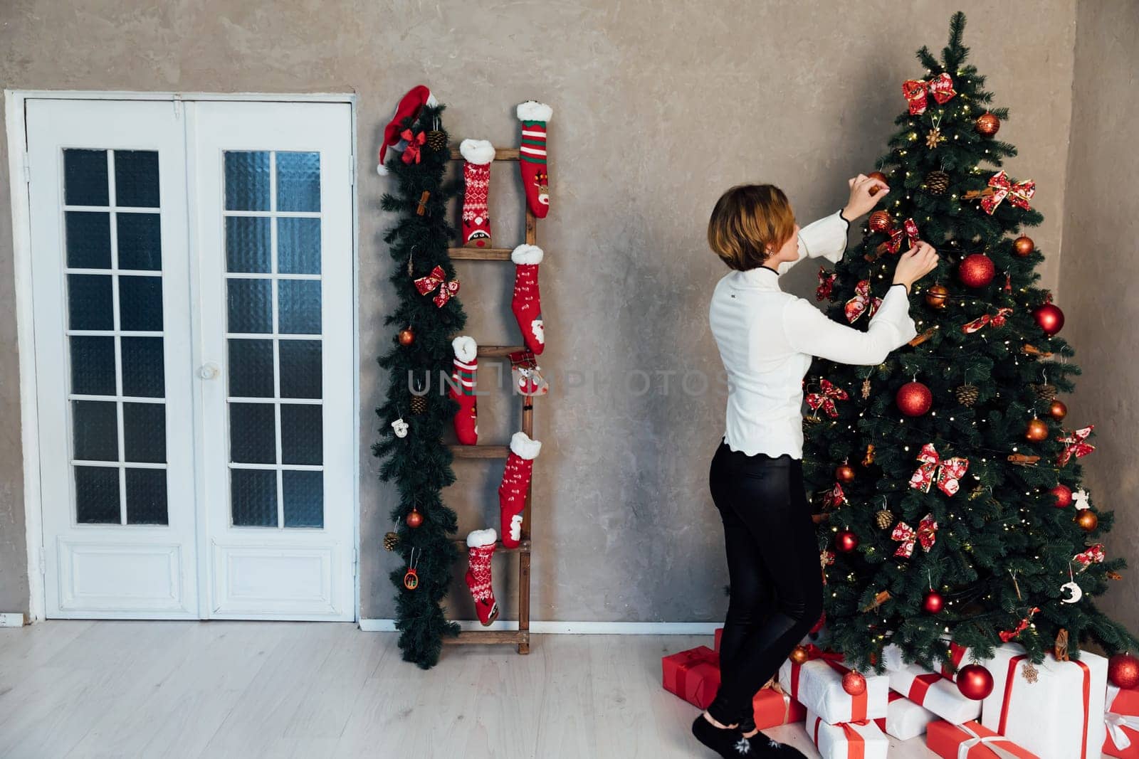 woman decorating christmas tree with gifts at home