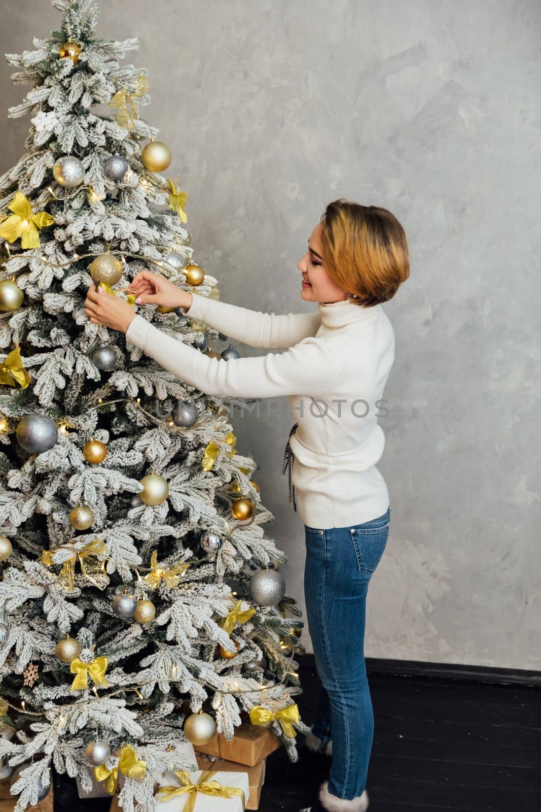 woman decorating christmas tree with gifts at home